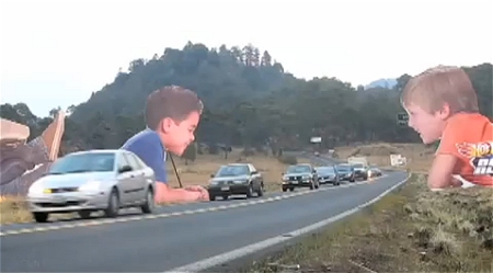 ↑ 公道を通り過ぎる自動車達の様子を楽しむかのように見える子供達の看板